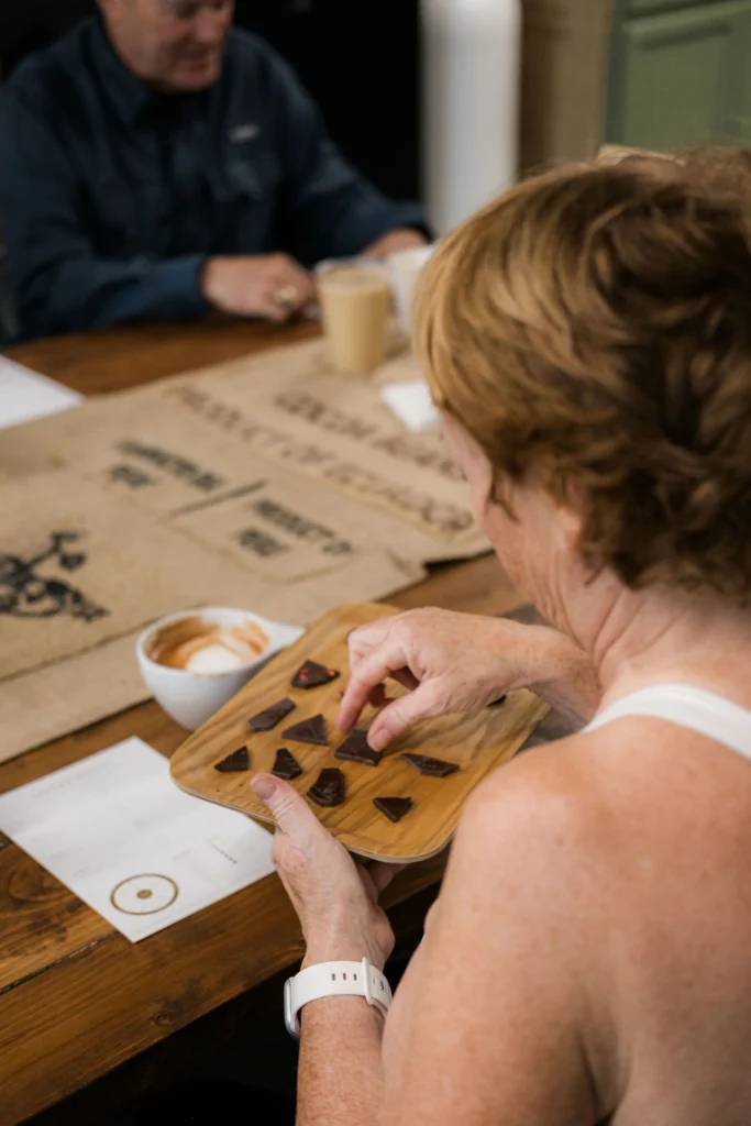 A woman participates in a gourmet chocolate tasting in Park City, selecting artisan dark chocolate pieces from a wooden tray during a culinary workshop.