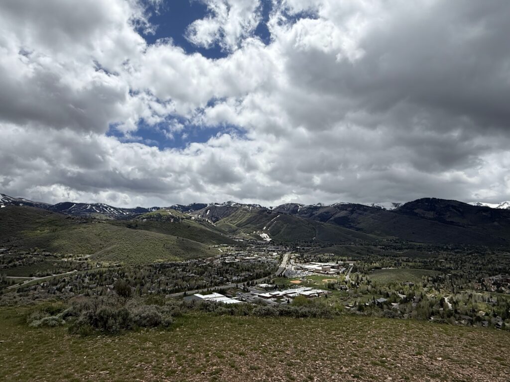 Panoramic view of Park City Utah mountains with ski runs, green hills, and dramatic clouds in spring.