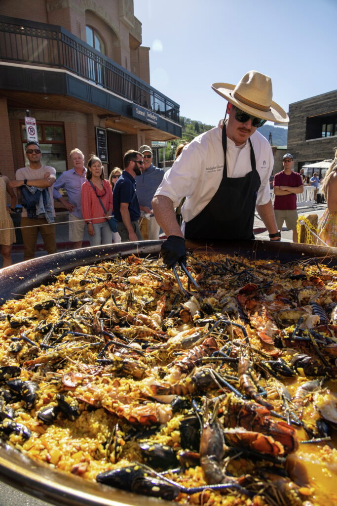 Executive Chef Christopher Gibson of Deer Valley prepares a massive seafood paella with lobster, prawns, and mussels in an eight-foot wide pan on Main Street during Savor the Summit, showcasing premium Deer Valley dining.