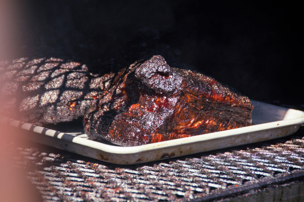 A close-up of a perfectly smoked, deeply caramelized brisket on a tray inside a live-fire smoker, showcasing Chef Ryan Arensdorf's signature style for the Taste of Luxury series.