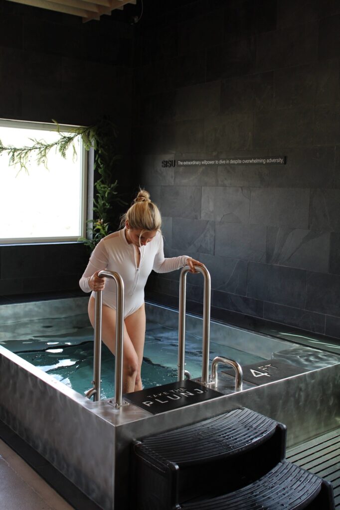 A woman in a white swimsuit steps into a cold plunge tub at Plunj Park City, a top destination for recovery after visiting best restaurants in Park City or exploring historic Park City.