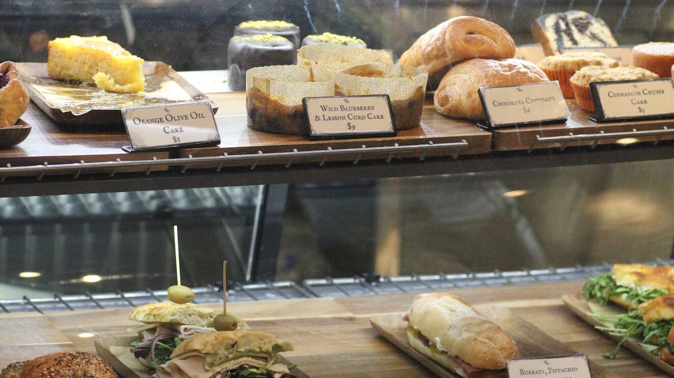 Freshly prepared turkey avocado sandwiches, gourmet baguettes, and orange olive oil cake inside the display case at The Olive Press Cafe, highlighting premier food in Park City area day trips.